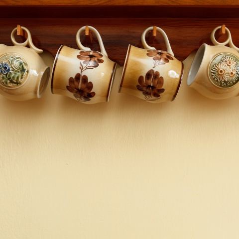 Kubki ceramicne wiszące pod drewnianą półką. 