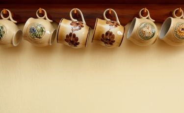 Kubki ceramicne wiszące pod drewnianą półką. 